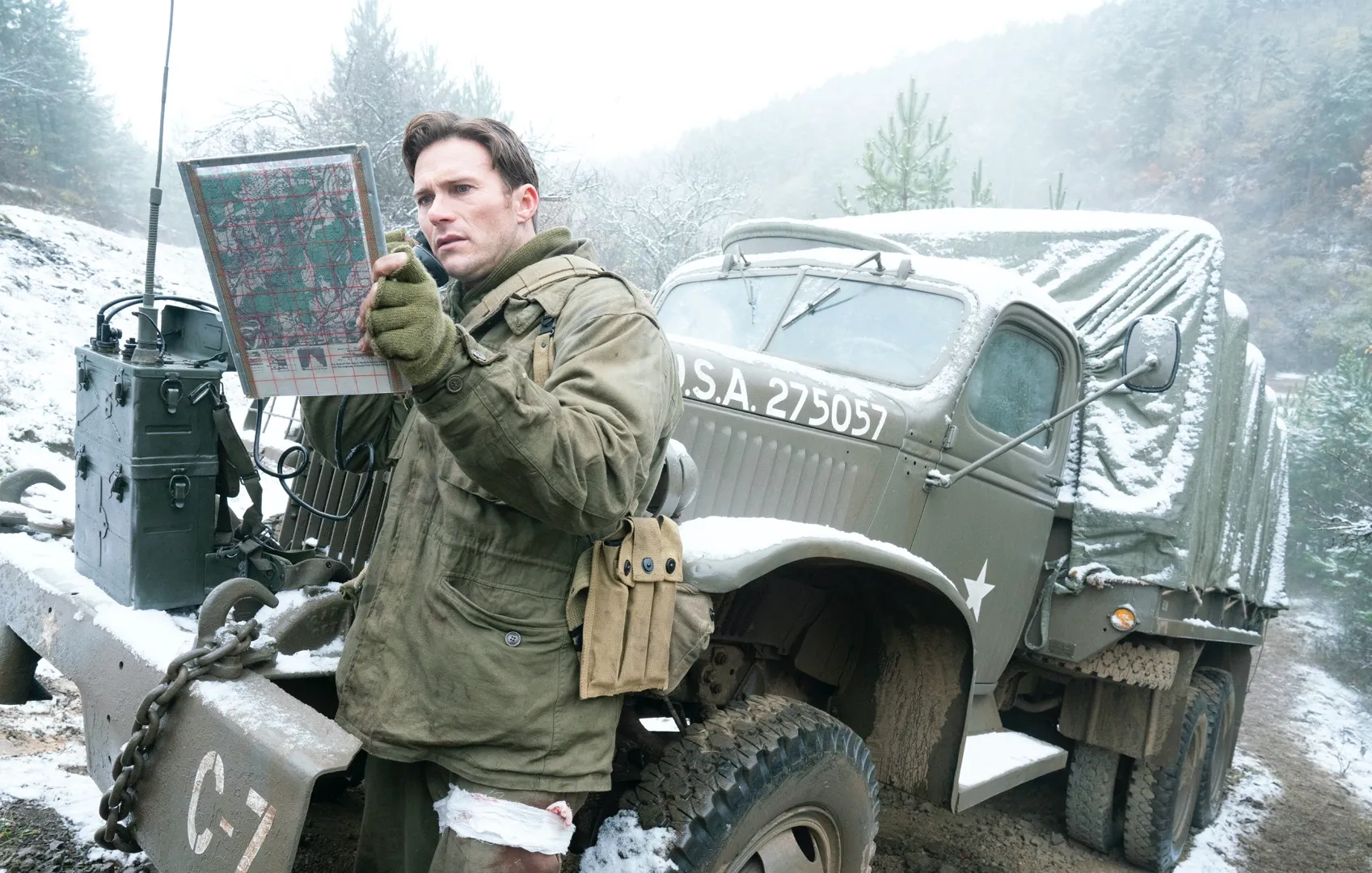 A soldier looking at a map, leaning up against a truck.