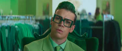 A man in green sits in an office with a concerned look on his face.