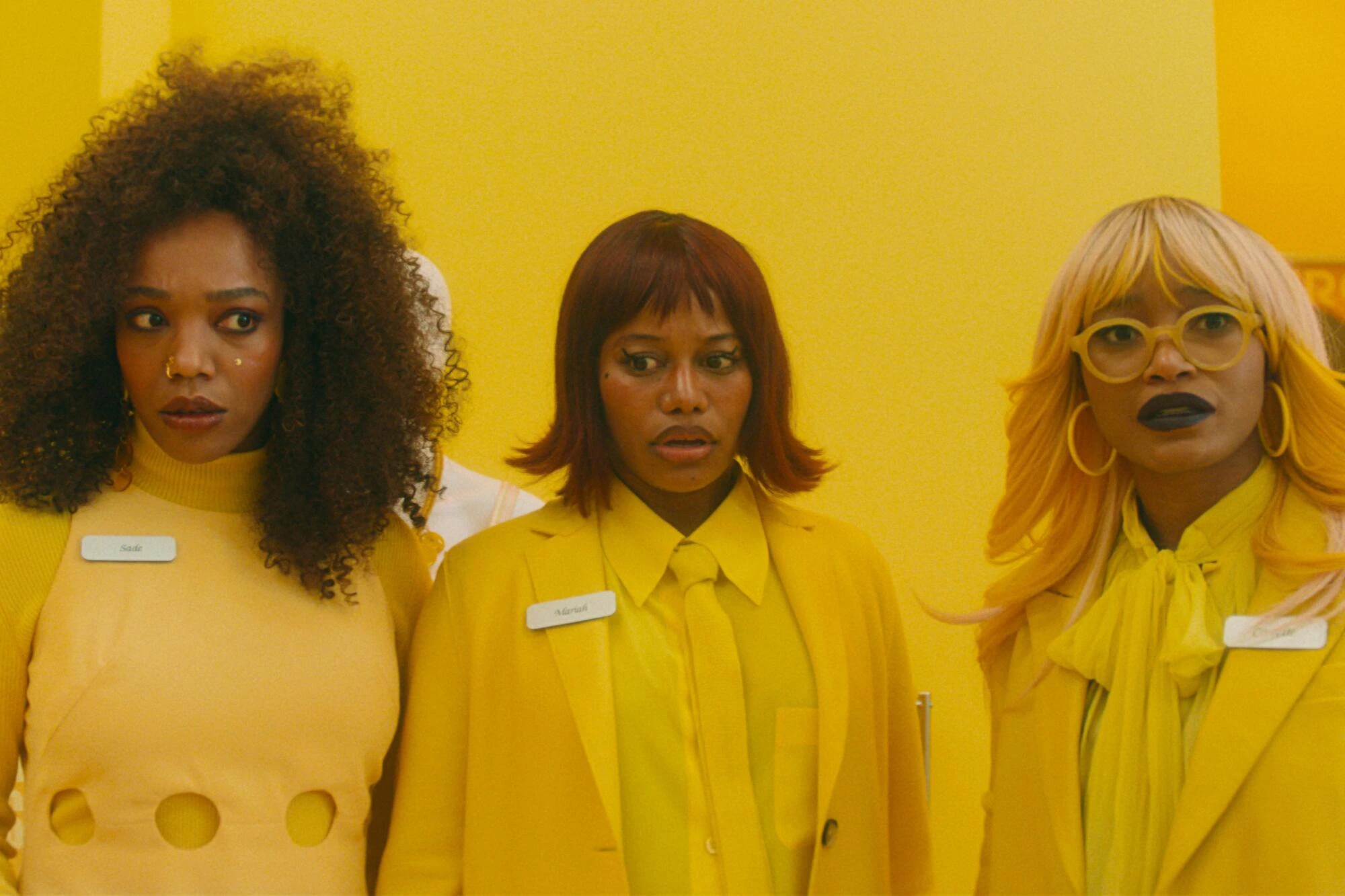 Scene from I Love Boosters. Three women stand side-by-side in yellow outfits.