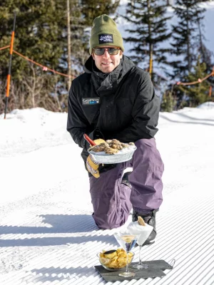 The Oyster Guy kneels on a ski slope with an entrée of oysters and martinis.