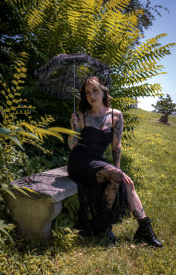 Cupcake Addams sitting on a bench and holding an umbrella at a cemetery