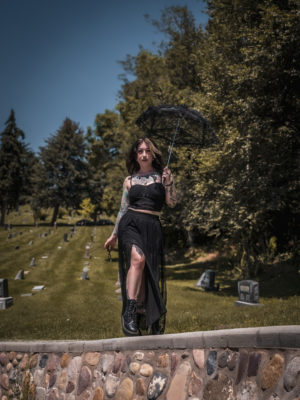 Cupcake Addams holding an umbrella at a cemetery