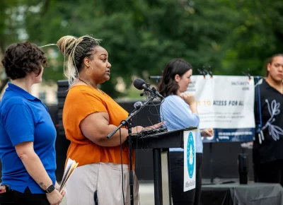 Salt Lake City's ADA Coordinator, Angela Haylock, speaks at a microphone during the ADA Day celebration with UTA at City Hall on July 27, 2026.